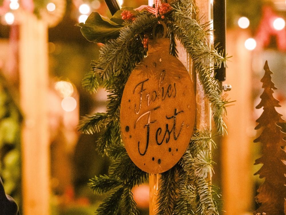 Weihnachtlich geschmückter Marktstand mit Tannenzweig und Anhänger mit der Aufschrift "Frohes Fest".