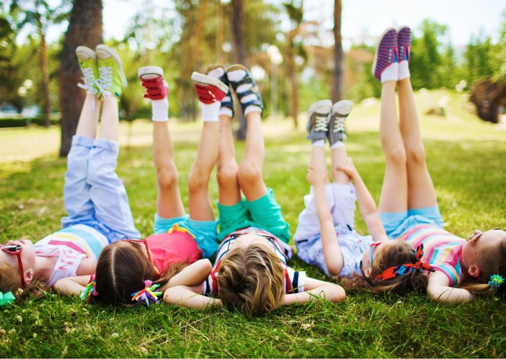 Fünf Kinder liegen auf dem Rücken im grünen Gras.