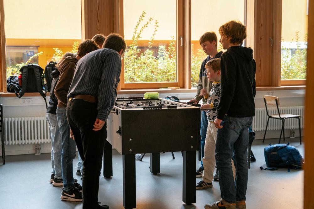 Jugendliche spielen Tischkicker. Ein Erwachsener schaut zu.