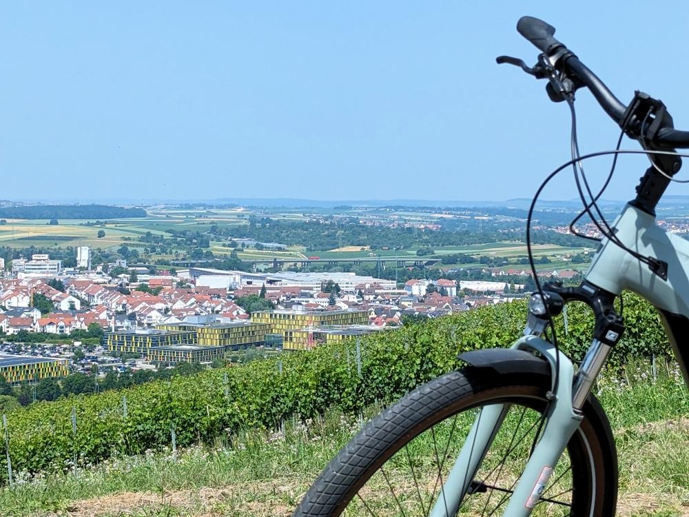 Im Vordergrund ist die vordere Hälfte eines Fahrrads zu sehen. Im Hintergrund sieht man Winnenden  von oben. In der Mitte ist das Rems-Murr-Klinikum sichbar.