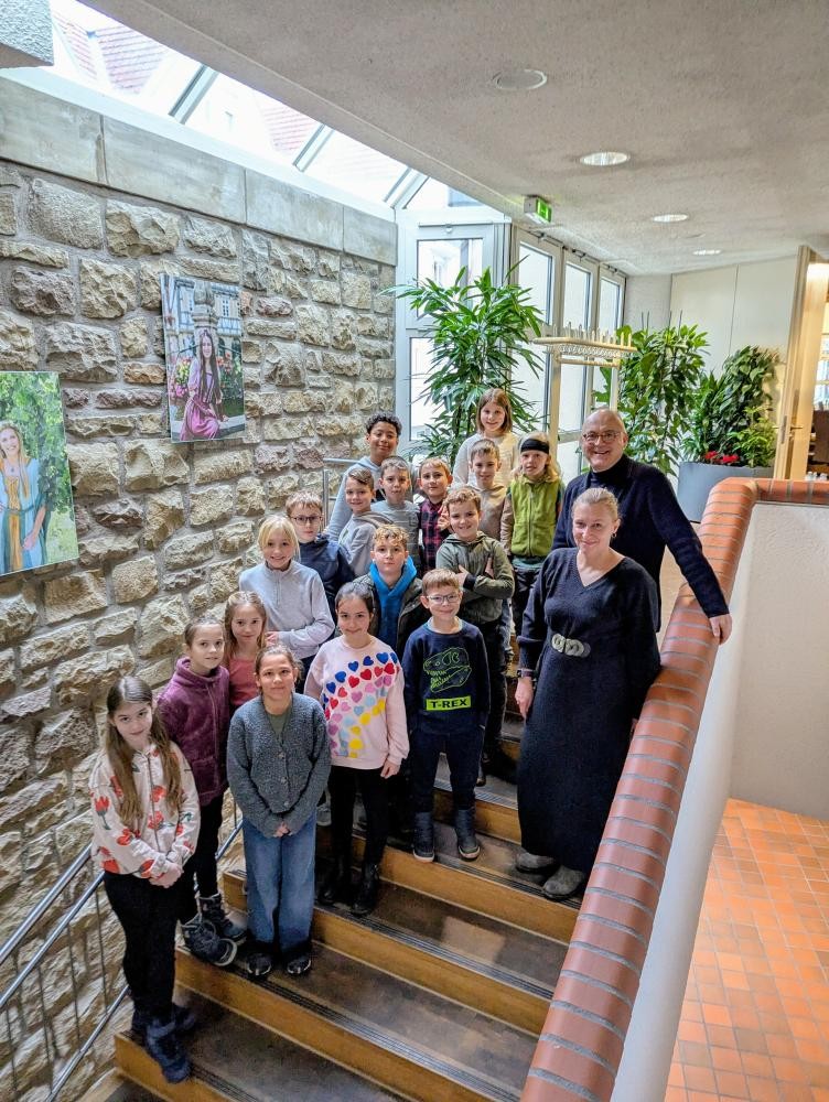 Gruppe von Kindern und zwei Erwachsenen steht auf einer Treppe in einem Gebäude mit Steinwand und Pflanzen