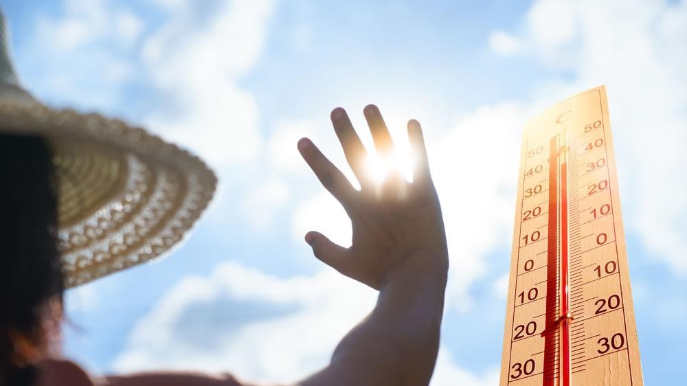 Hand mit gespreizten Fingern vor der Sonne und blauem Himmel sowie Thermometer