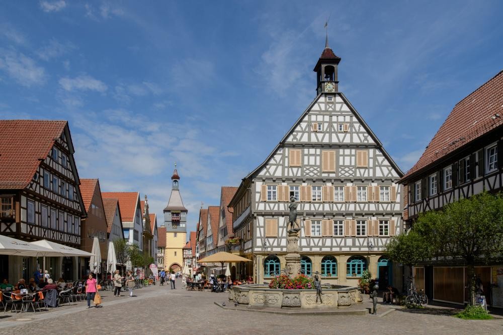 Historische Fachwerkhäuser an einem belebten Marktplatz mit Brunnen und Menschen in der Innenstadt