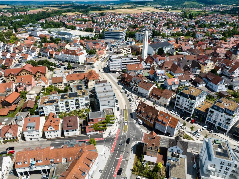 Luftaufnahme einer Stadt mit dicht bebauten Straßen, roten Dächern und einem hohen Schornstein in der Bildmitte