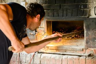 Ein Mann schiebt den Salzkuchen auf einem Blech in den Ofen des Backhauses