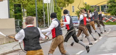 Junge Männer mit Peitschen beim sogenannten "Schnalzen" in einer Reihe. Die Peitschen mit Puscheln an den Enden werden durch die Luftgeschwungen