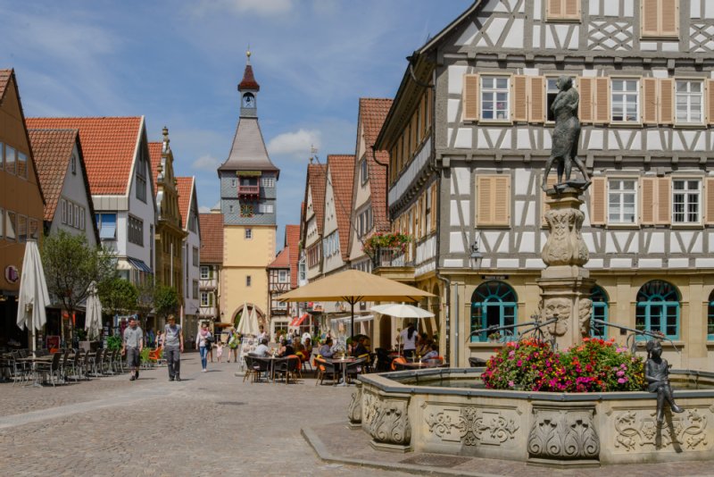 Der Marktbrunnen mit den Brunnenfiguren und pinken Blumen am Boden der mittleren Säule