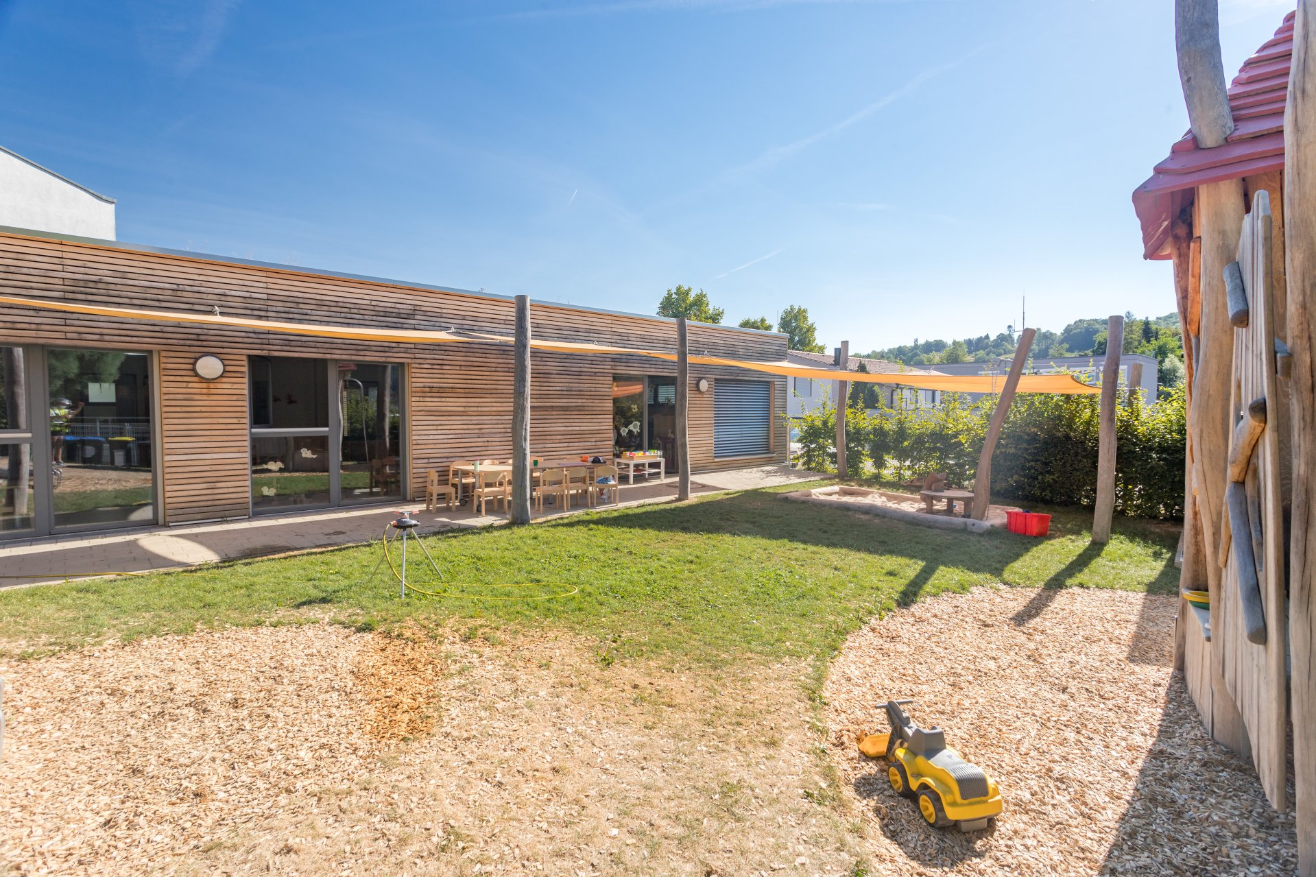 Der Außenbereich eines Winnender Kindergartens mit Spielgerüst, Sandkasten, Sonnensegel und Bastelecke