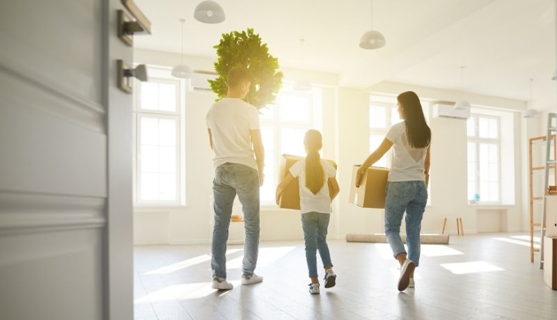 Familie zieht mit Kartons und Pflanze in eine leere Wohnung.