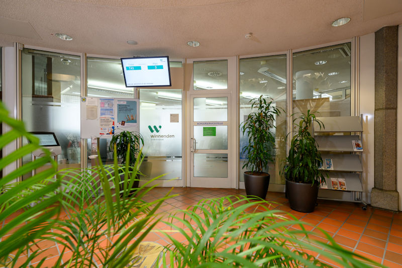 Eingang zur Bürgerservicestelle, daneben der Bildschirm mit der Anzeige der aktuell aufgerufenen Terminnummern