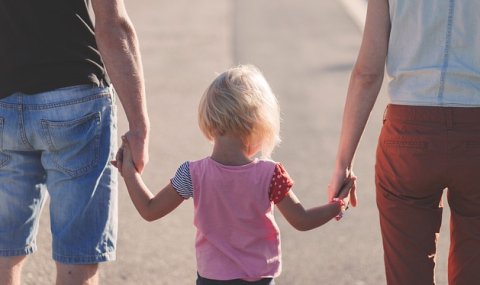 Wir sehen drei Personen, einen Mann, eine Frau und ein kleines Mädchen, von hinten. Sie halten sich an den Händen.