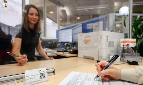 Eine Mitarbeiterin der Bürgerservicestelle bedient eine Kundin, die mit einem Stift einen Antrag unterschreibt.