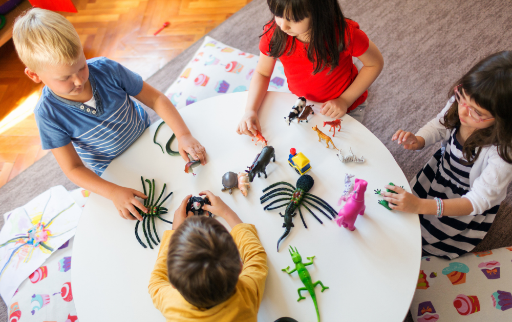 Kinder sitzen um einen runden Tisch und spielen mit verschiedenen Tierfiguren aus Kunststoff