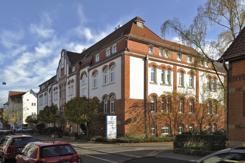 Seitenansicht des Gebäudes der Paulinenpflege in Winnenden. Roter Backstein fasist bis zu den Fenstern im ersten Stock zu sehen. Daraufhin folgt die strahlend weiße Fassade, welche weiter oben vom ebenso roten Dach abgedeckt wird.