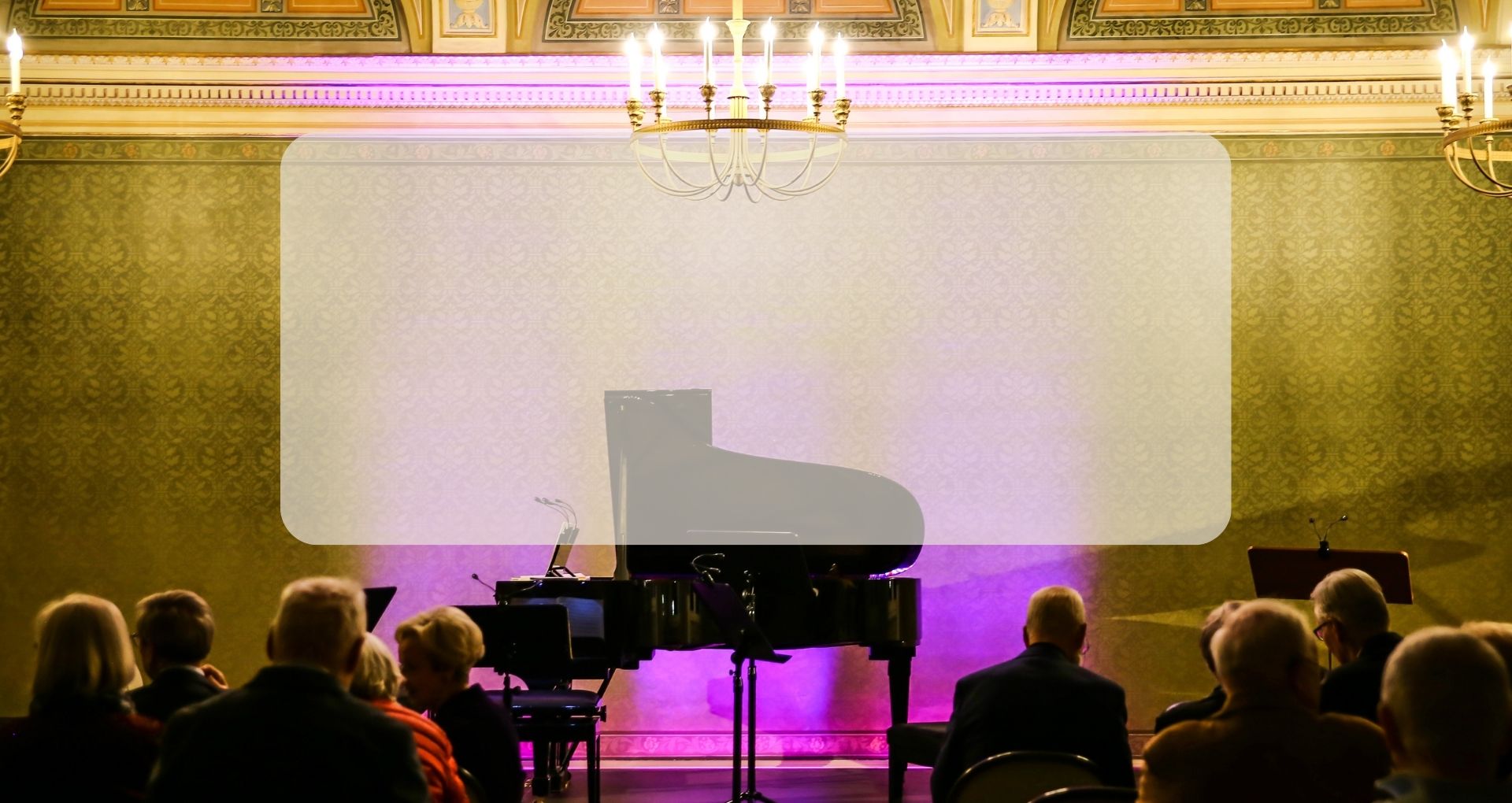 ImKonzertsaal des Schloss Winnenden steht ein Flügel vor den Zuschauerinnen und Zuschauern. Darüber hängt ein Kronleuchter