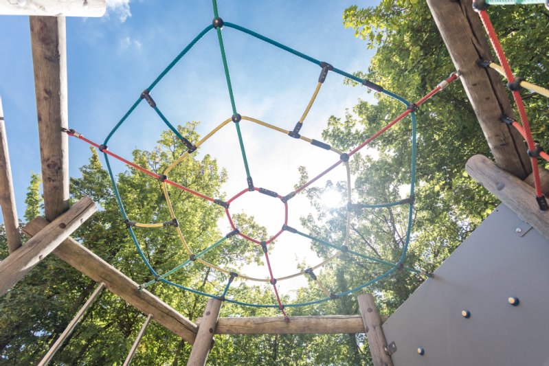 Ein Kletternetz von unten fotografiert, sodass durch die Löcher des Netzes die Bäume und die Sonne zu sehen sind.