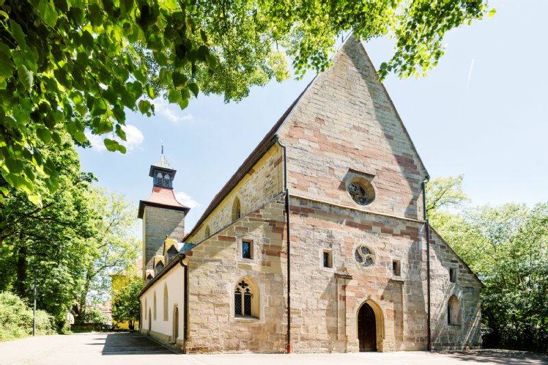 Die Schlosskirche Winnenden leicht seitlich fotografiert. Die Sonne erhellt die Front der Kirche mit den kleinen verzierten Fenstern.