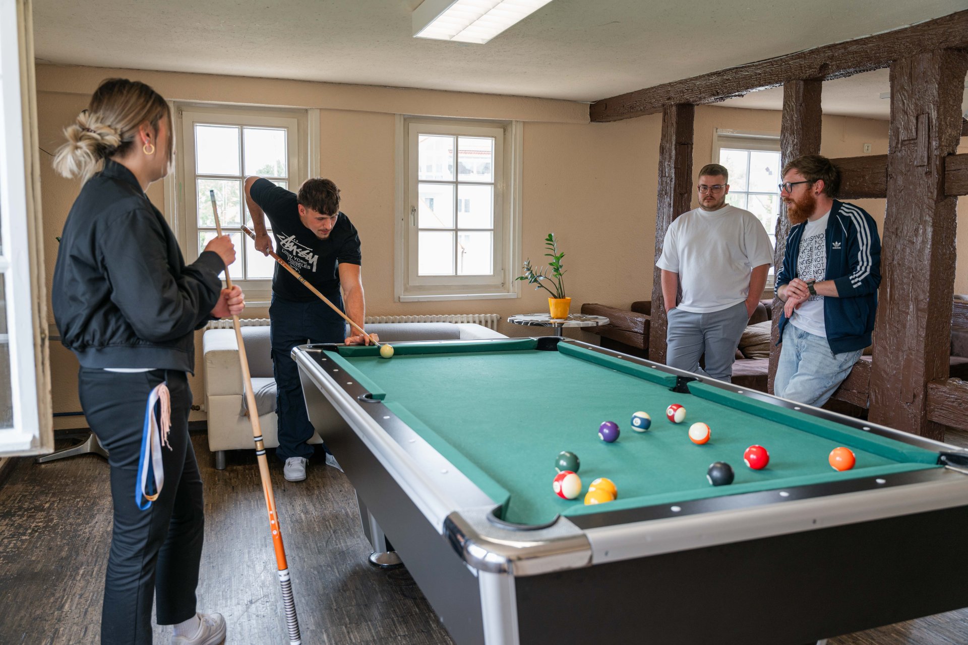 Vier junge Menschen spielen zusammen Billard im Jugendzentrum.
