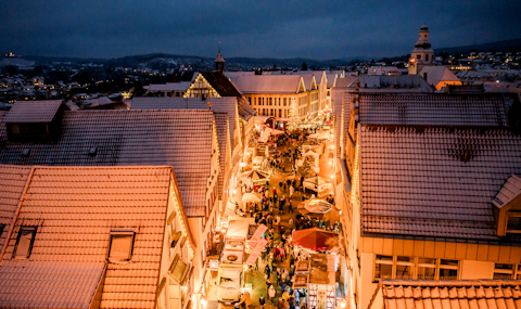 Blick vom Torturm auf den Winnender Weihnachtsmarkt bei Nacht. Neben erhellten Dächern durch die Fasadenbeleuchtung sind die Stände und Besucher zu sehen