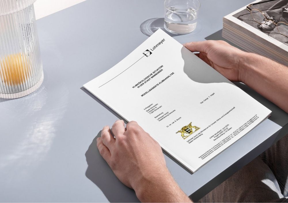 Symbolfoto: Der Bericht liegt auf einem grauen Tisch und wird mit der rechten Hand aufgeschlagen