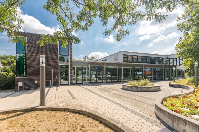 Zum Eingang Albertville-Realschule führen Treppen und eine Rampe. Die Front der Schule ist mit vielen bodentiefen Fenstern gestaltet. 