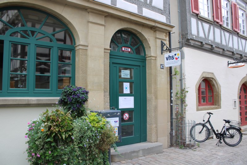 Eingang der Volkshochschule in der Mühltorstraße. An der Hauswand hängt das Schild mit dem Logo der vhs.