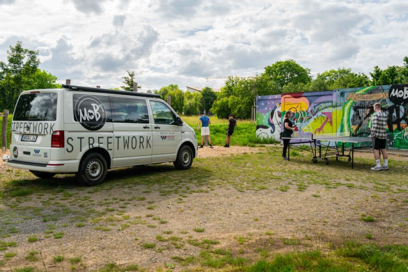 Im freien spiele Jugendliche an einer Tischtennisplatte. Daneben steht der Van der Streetworkarbeit