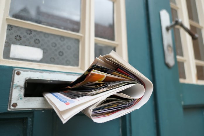 Sybolbild: Eine Zeitung steckt im Briefschlitz einer blauen Tür.