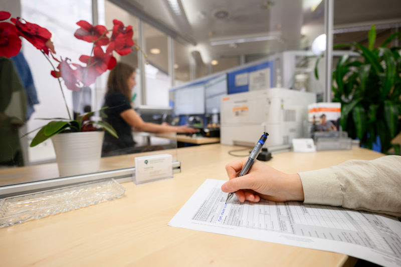 Ausfüllen eines Antrags in der Bürgerservicestelle. EIne Mitarbeiterin sitzt im Hintergrund am PC und bearbeitet den Antrag.